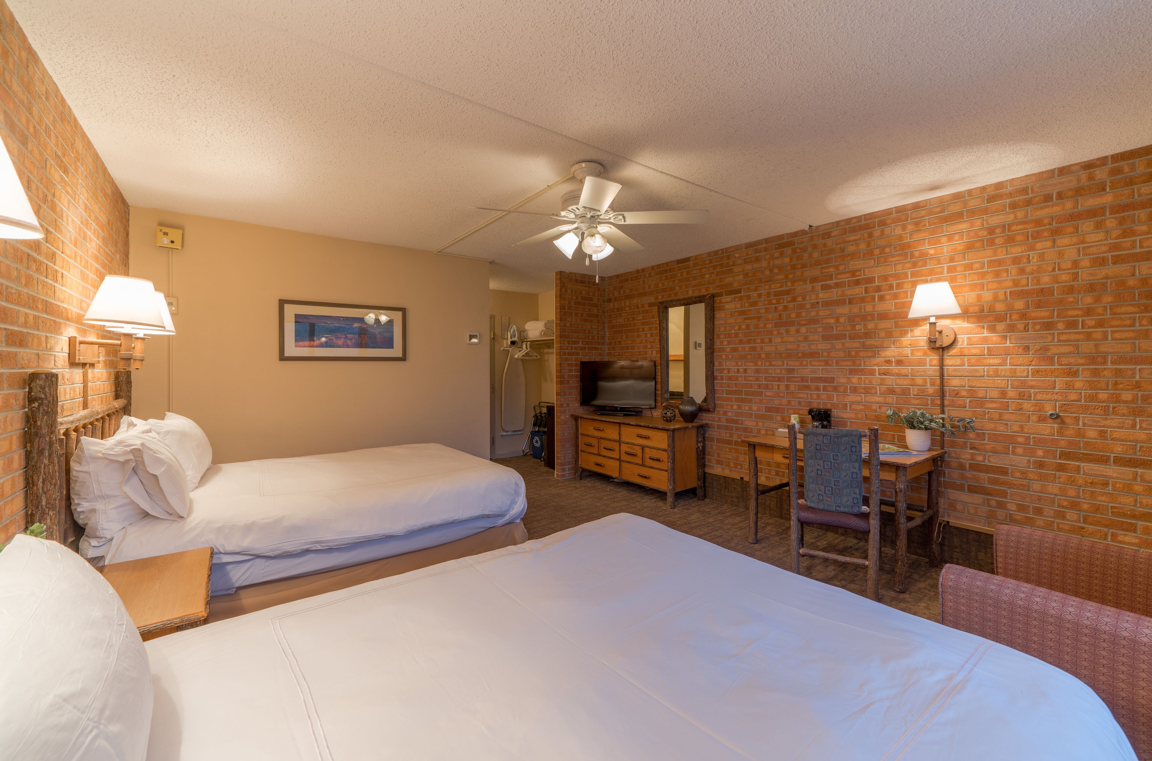 A hotel room with two beds, a TV, a desk with a chair, and a ceiling fan.
