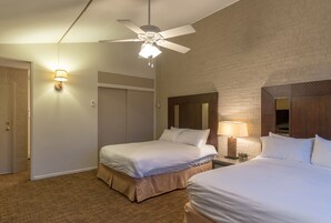 Habitación de hotel con dos camas, ventilador de techo, lámpara de pared y pared de ladrillo.