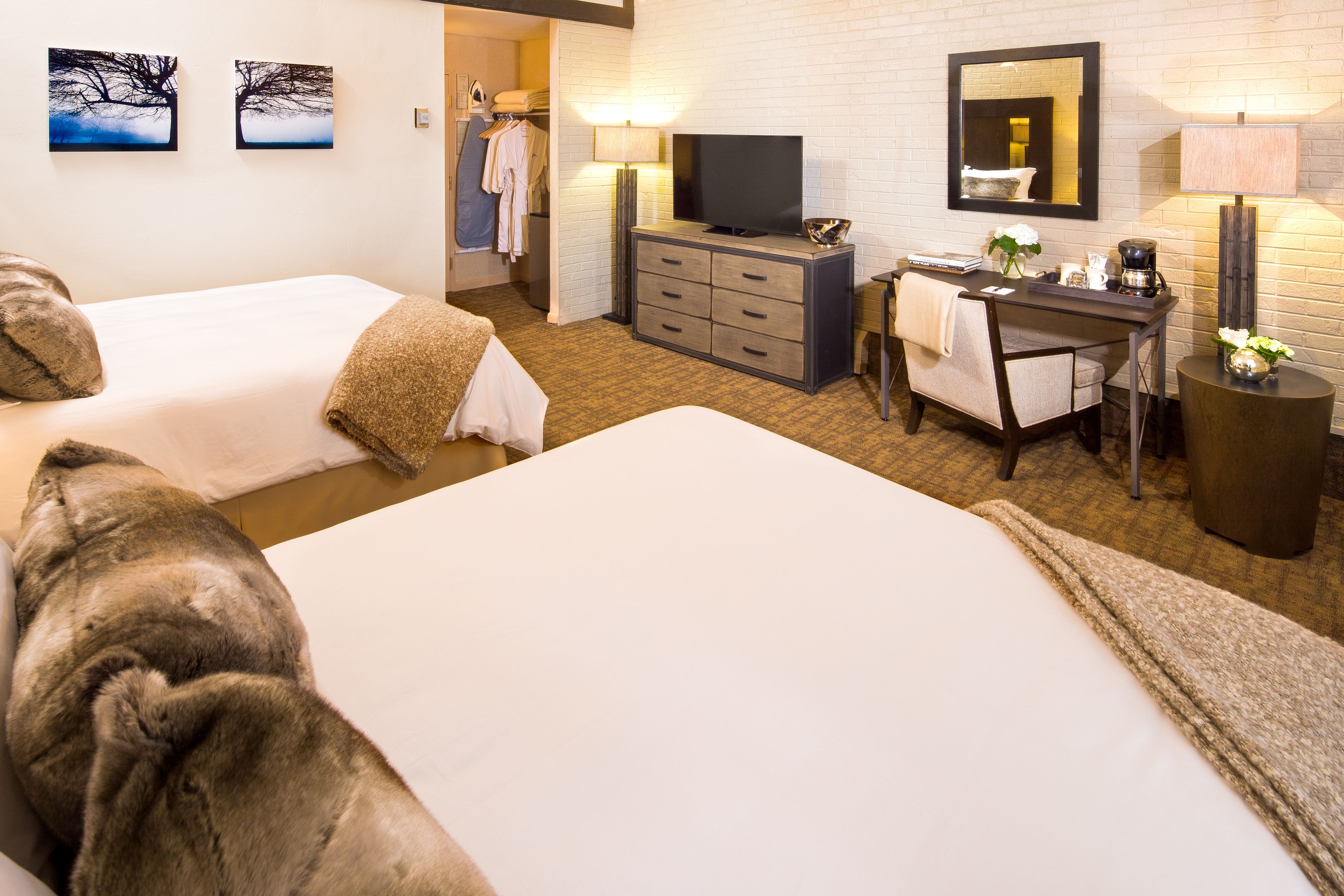 Hotelkamer met twee bedden, een bureau met stoel, een televisie, een spiegel en een bijzettafeltje met lamp en bloemen.
