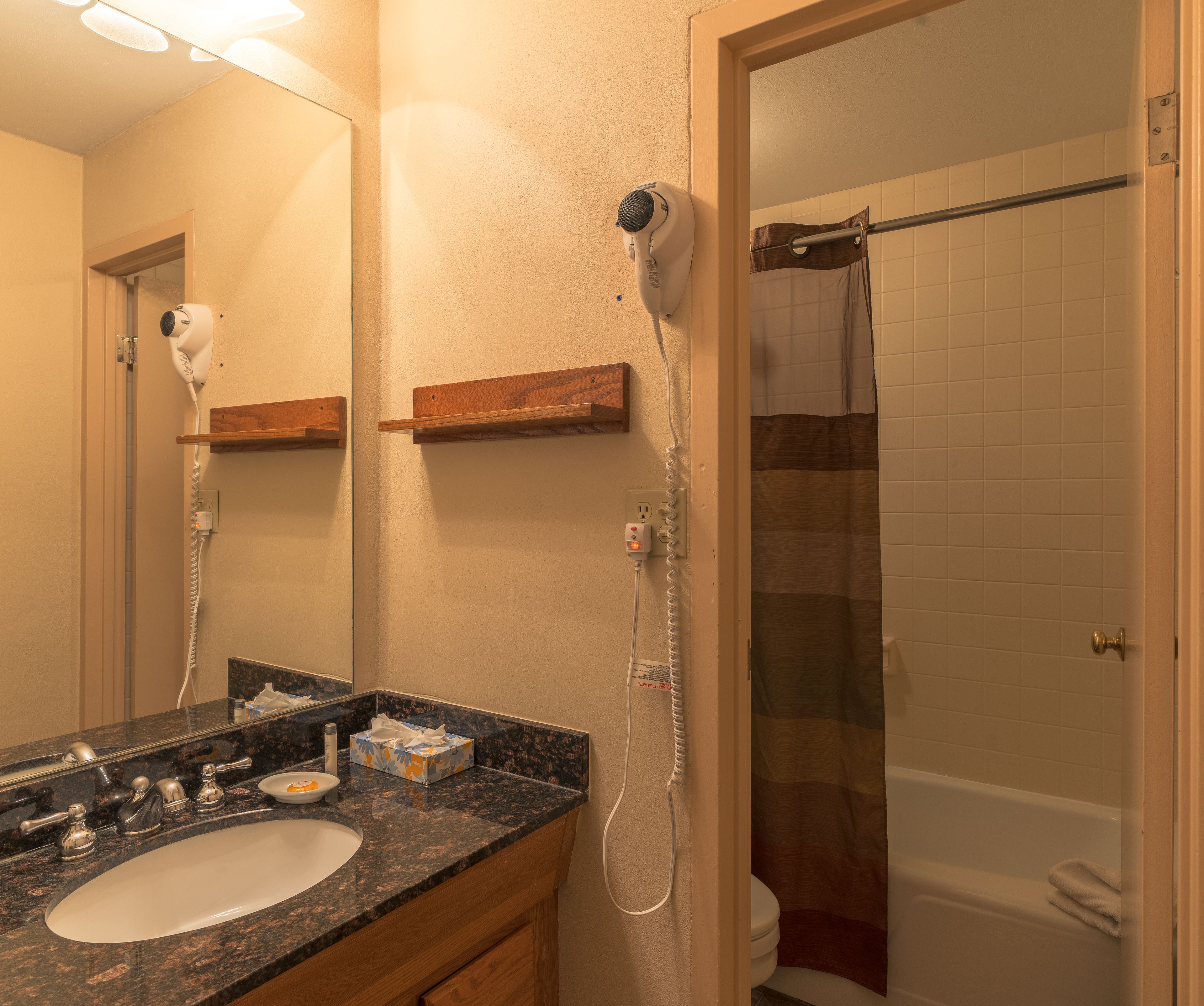 A bathroom with a sink, mirror, hairdryer, and shower.