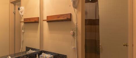 A bathroom with a sink, mirror, hairdryer, and shower.