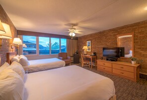 Habitación de hotel con dos camas, un escritorio, un televisor y un amplio ventanal con vistas a la montaña.