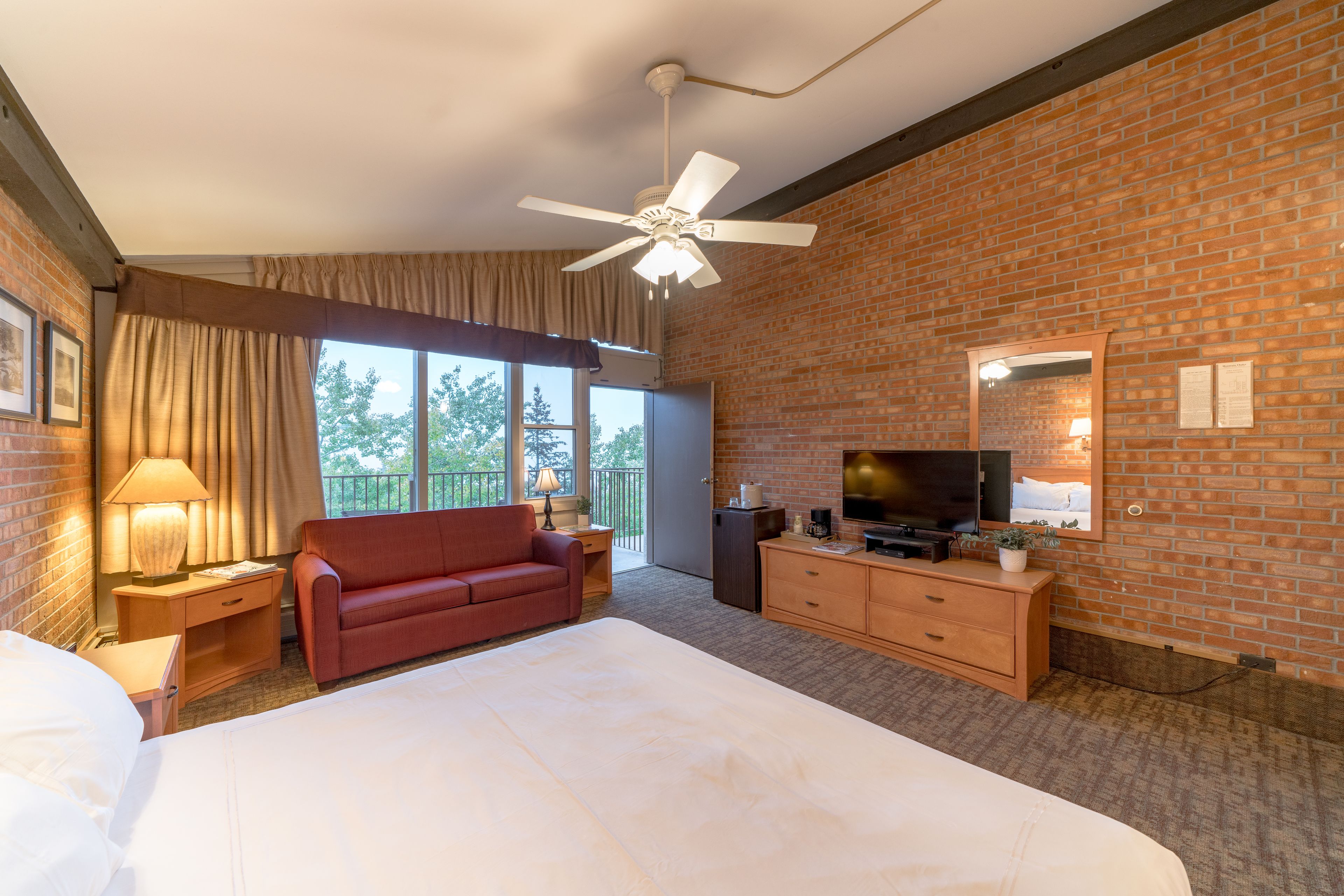 A hotel room with a large bed, a red sofa, a television, and a brick wall.