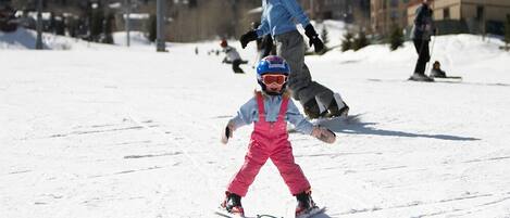 A ski slope with skiers and a child in pink ski gear.