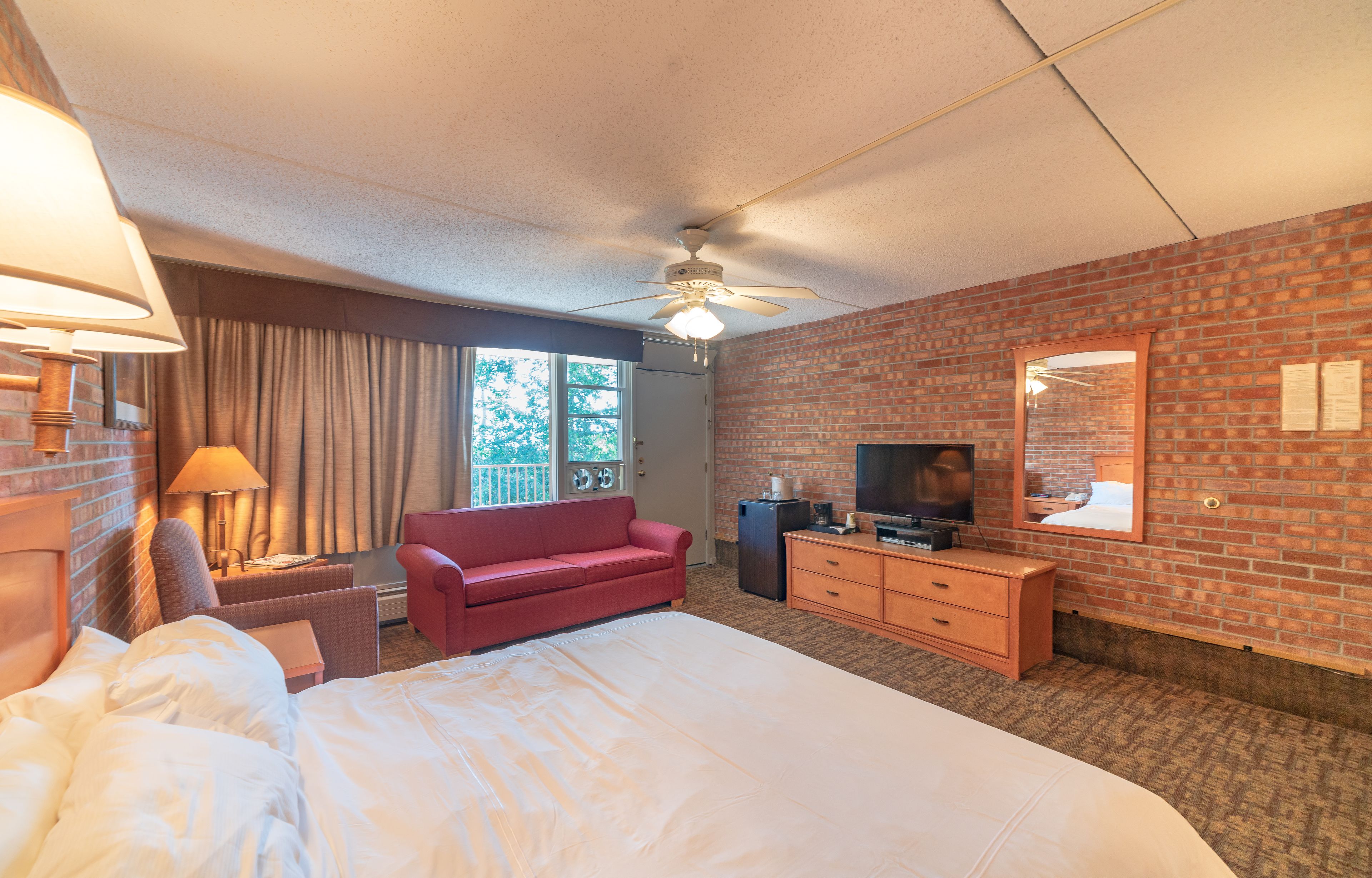 Une chambre d’hôtel avec un grand lit, un canapé rouge, une télévision, une commode et un ventilateur de plafond.