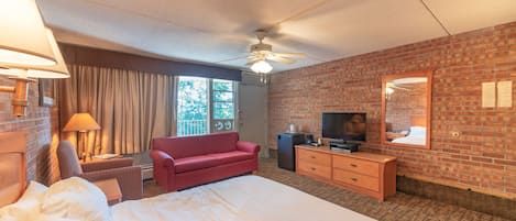 A hotel room with a large bed, a red sofa, a television, a dresser, and a ceiling fan.