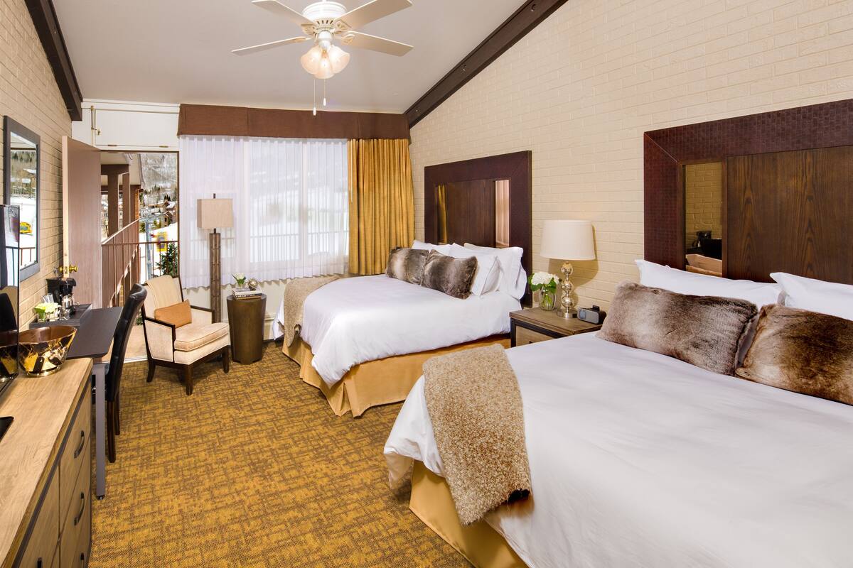 Une chambre d’hôtel avec deux lits, un bureau, une chaise, une lampe et un ventilateur de plafond.