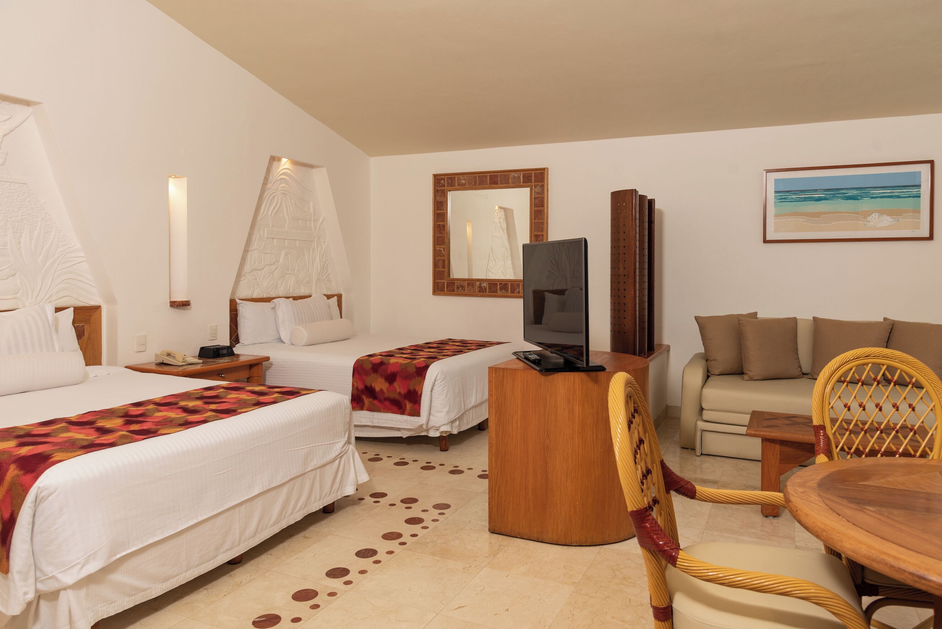 A hotel room with two beds, a television, a sofa, a dining table, and a beach-themed painting.
