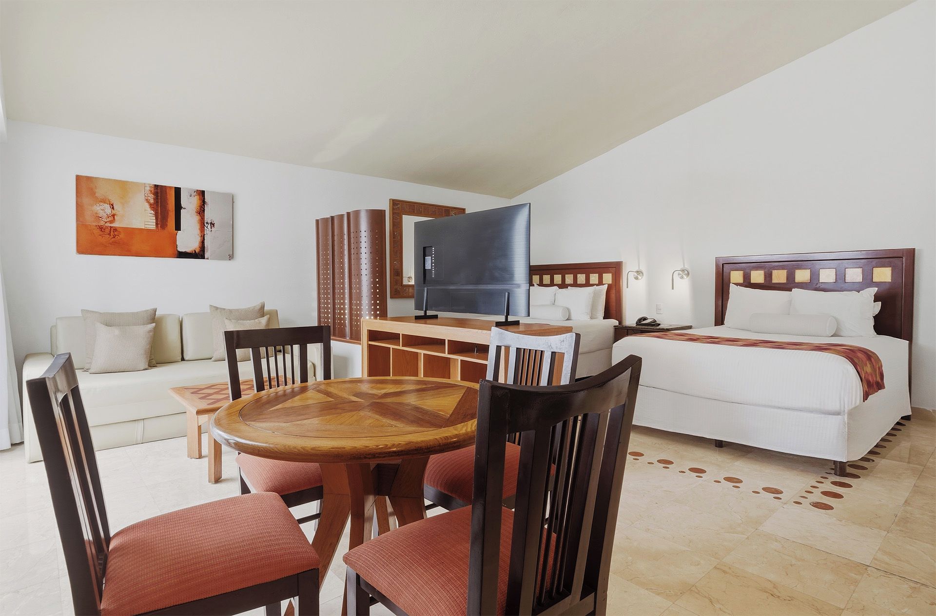 Una habitación de hotel con cama, televisión, zona de comedor con sillas y mesa, y un sofá.