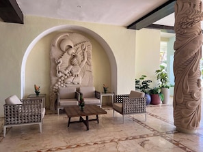 A lobby with a stone relief, two wicker armchairs, a wooden coffee table, and a potted plant. - Sunset Fishermen Beach Resort (Playa del Carmen)