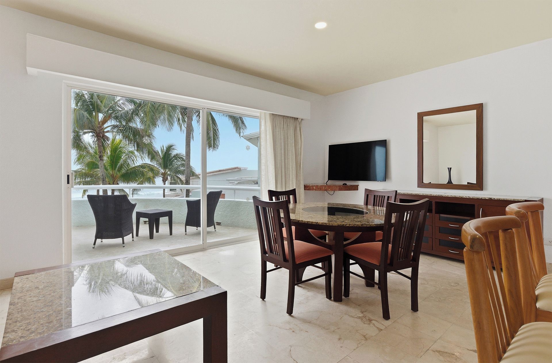 A dining area with a glass table, chairs, and a television on the wall.