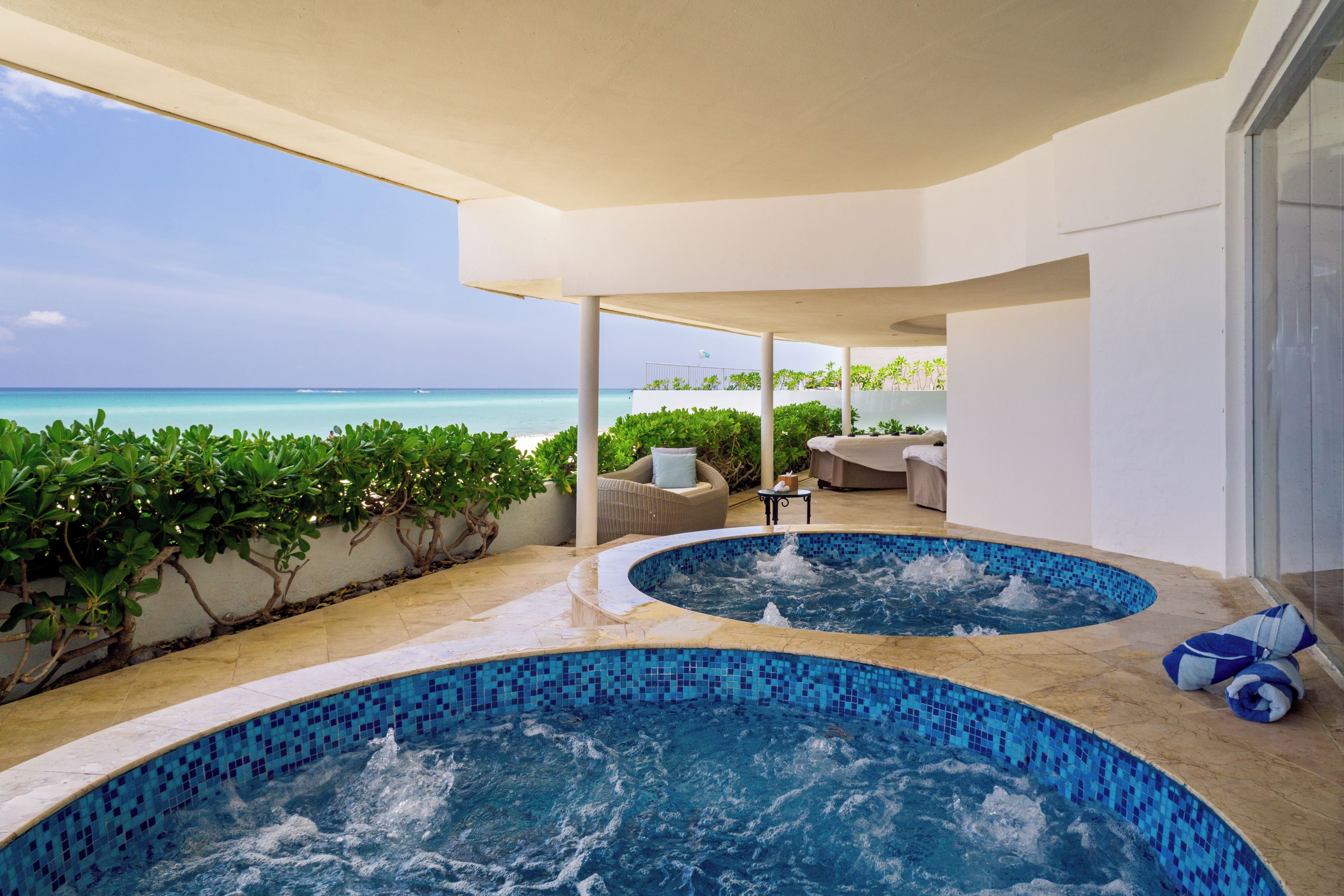 A pool area with two hot tubs, a seating area, and a view of the ocean.