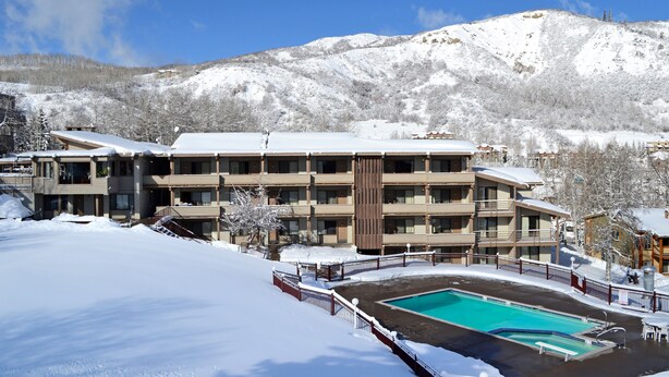 A hotel with multiple floors, a swimming pool, and a snowy mountainous backdrop. - Pokolodi Lodge (Snowmass Village)
