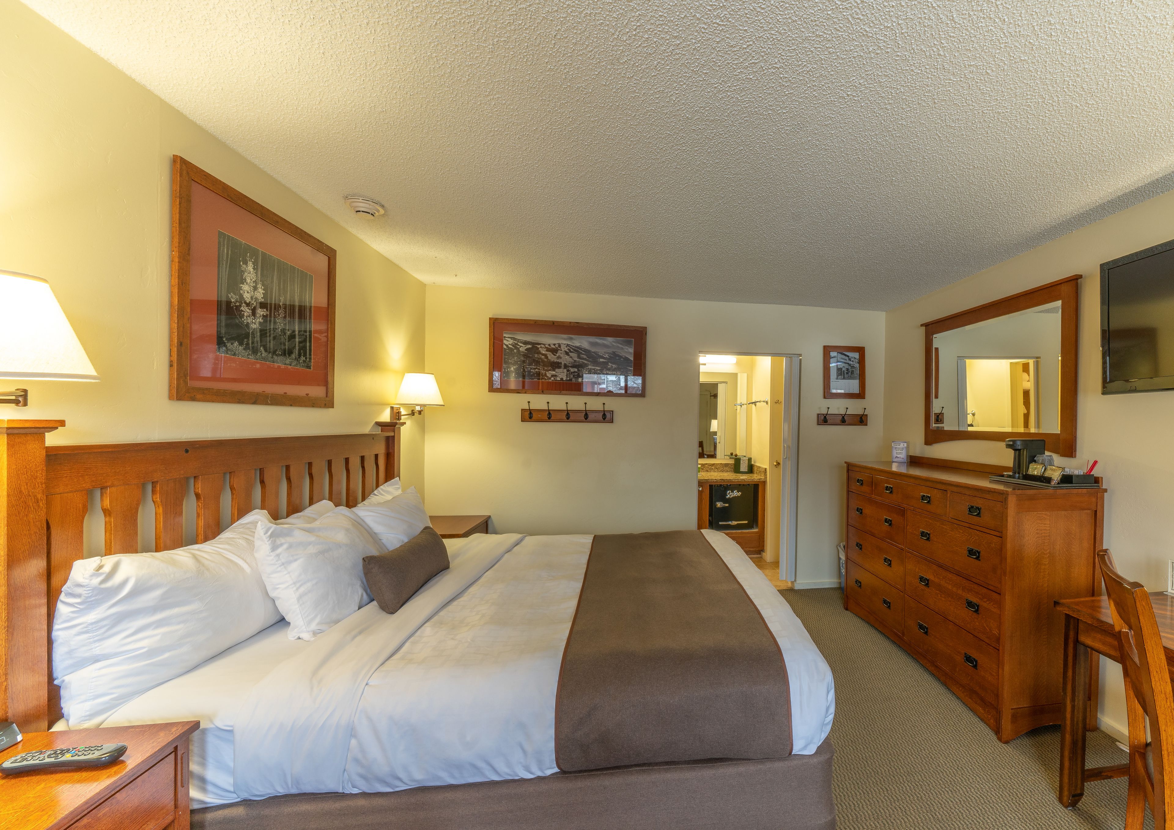 Ein Hotelzimmer mit einem großen Bett, einem Schminktisch, einem Spiegel und einem Fernseher.