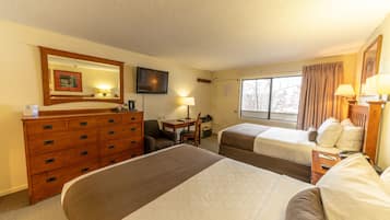 A hotel room with two beds, a dresser, a desk with a chair, a television, and a window with curtains.