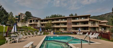 A hotel with a swimming pool, lounge chairs, and a view of the mountains.