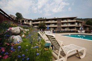 A poolside area with lounge chairs, a swimming pool, and a building with multiple balconies. - Pokolodi Lodge (Snowmass Village)