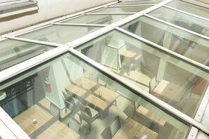 Een modern interieur met glazen dak, houten tafels en stoelen klaar voor een diner.