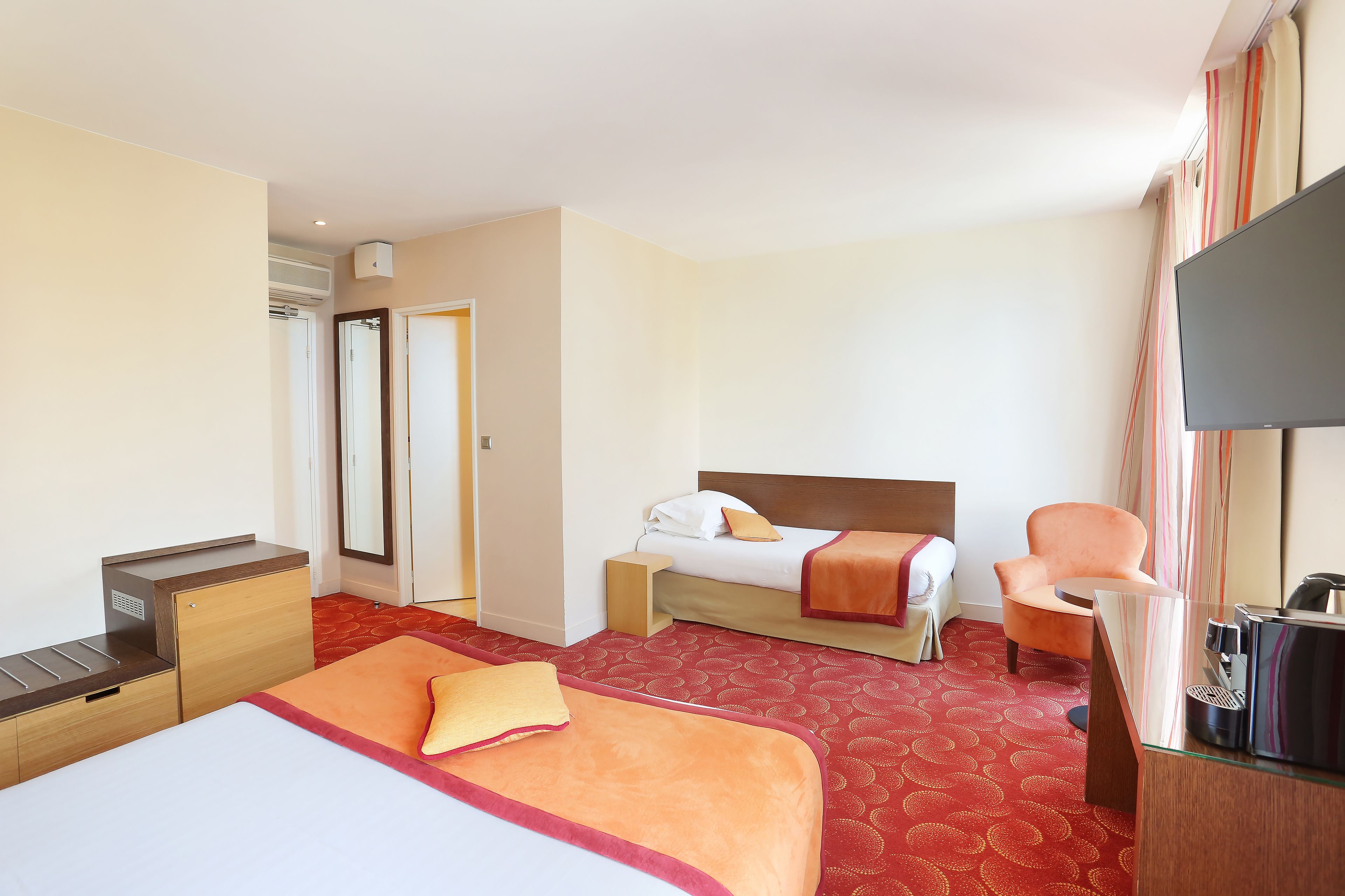 Habitación de hotel con dos camas, un escritorio, una silla y un televisor.