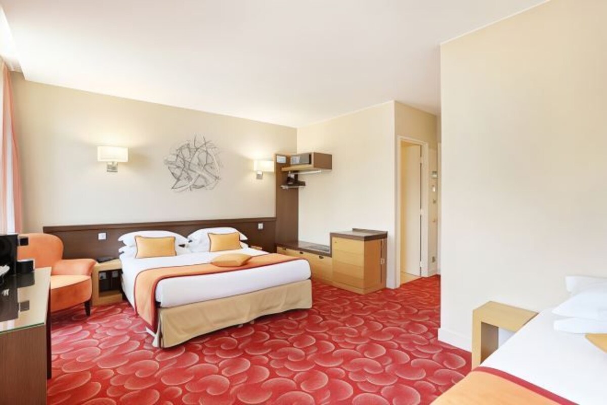 Habitación de hotel con cama, escritorio, silla, armario pequeño y televisor montado en la pared.