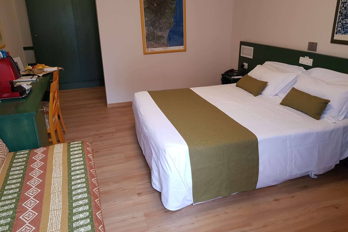 Une chambre d’hôtel avec un grand lit, un bureau avec une chaise, un mur vert et une carte encadrée.