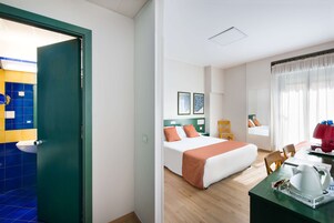 Una habitación de hotel con cama, escritorio con hervidor, silla y ventana con cortinas.