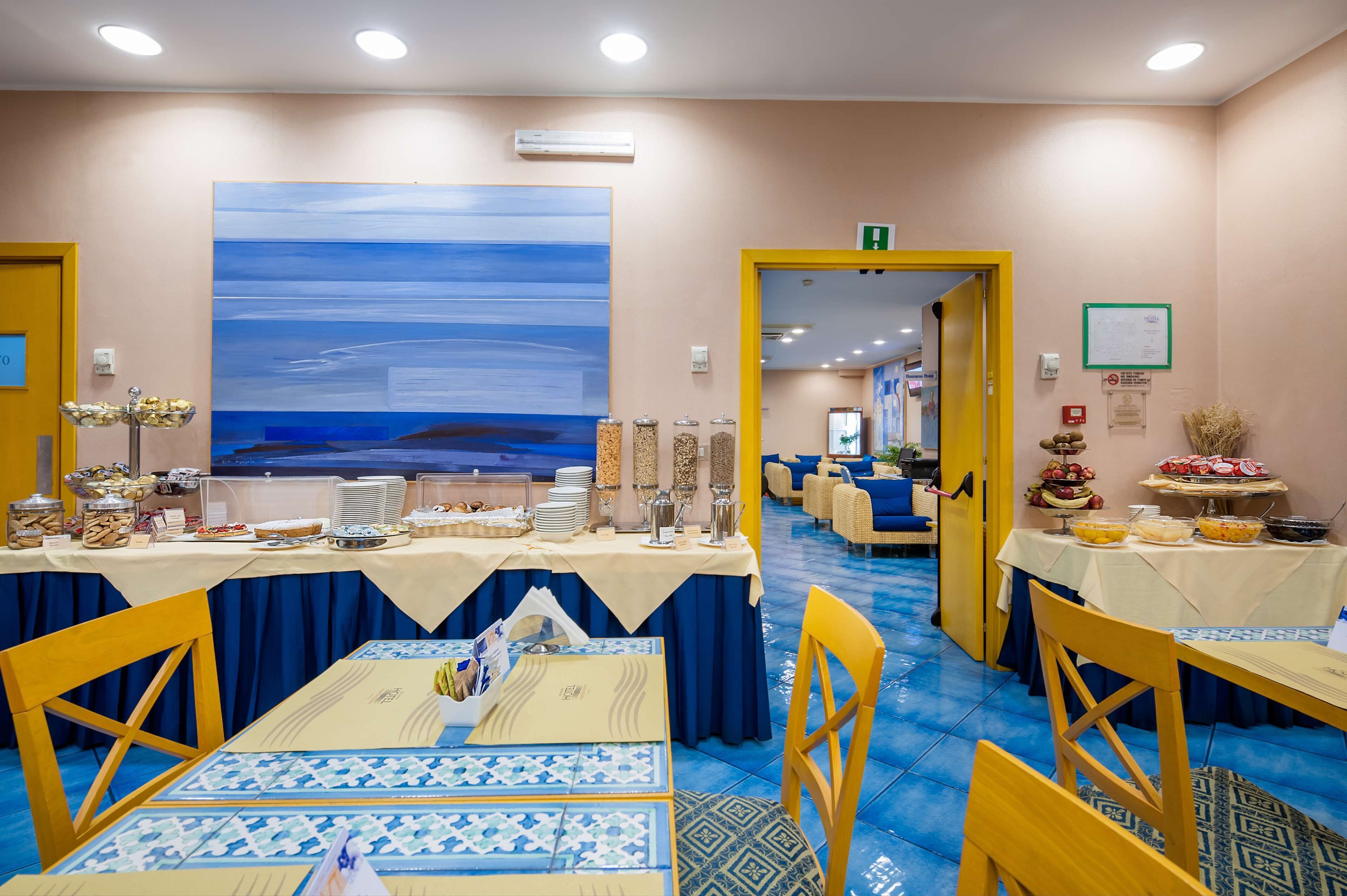 A dining area with tables set for a meal, a large abstract painting on the wall, and a yellow door leading to another room.