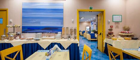 A dining area with tables set for a meal, a large abstract painting on the wall, and a yellow door leading to another room.