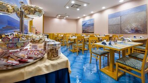 Un espace repas avec des tables et des chaises, un buffet proposant divers plats, et des luminaires au plafond.