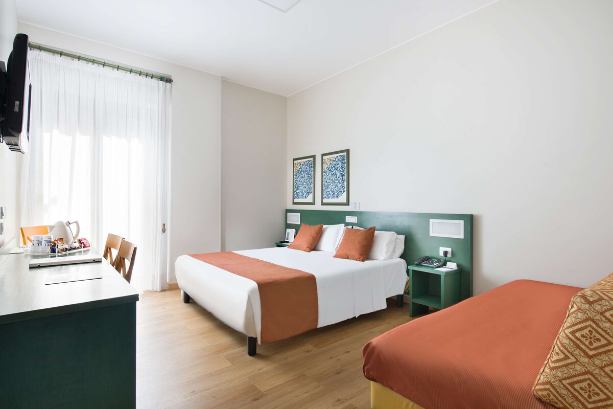 Une chambre d’hôtel avec un lit, une table de chevet et un bureau avec une lampe.