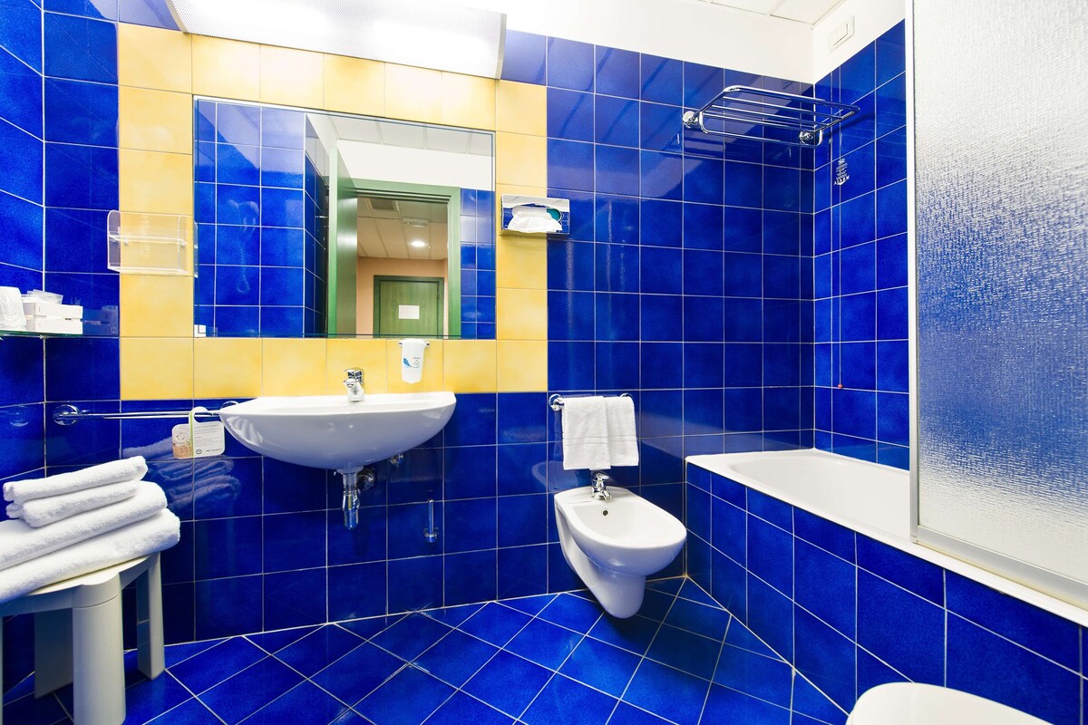Une salle de bain avec des carreaux bleus, un lavabo blanc, un bidet et un miroir.