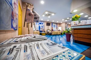 Un vestíbulo de hotel con periódicos sobre una mesa, un mostrador de recepción y piso azul.