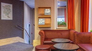 A corner seating area with a brick-patterned bench and two round tables, a framed map on the wall, and a window with orange curtains.