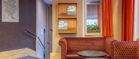 A corner seating area with a brick-patterned bench and two round tables, a framed map on the wall, and a window with orange curtains.