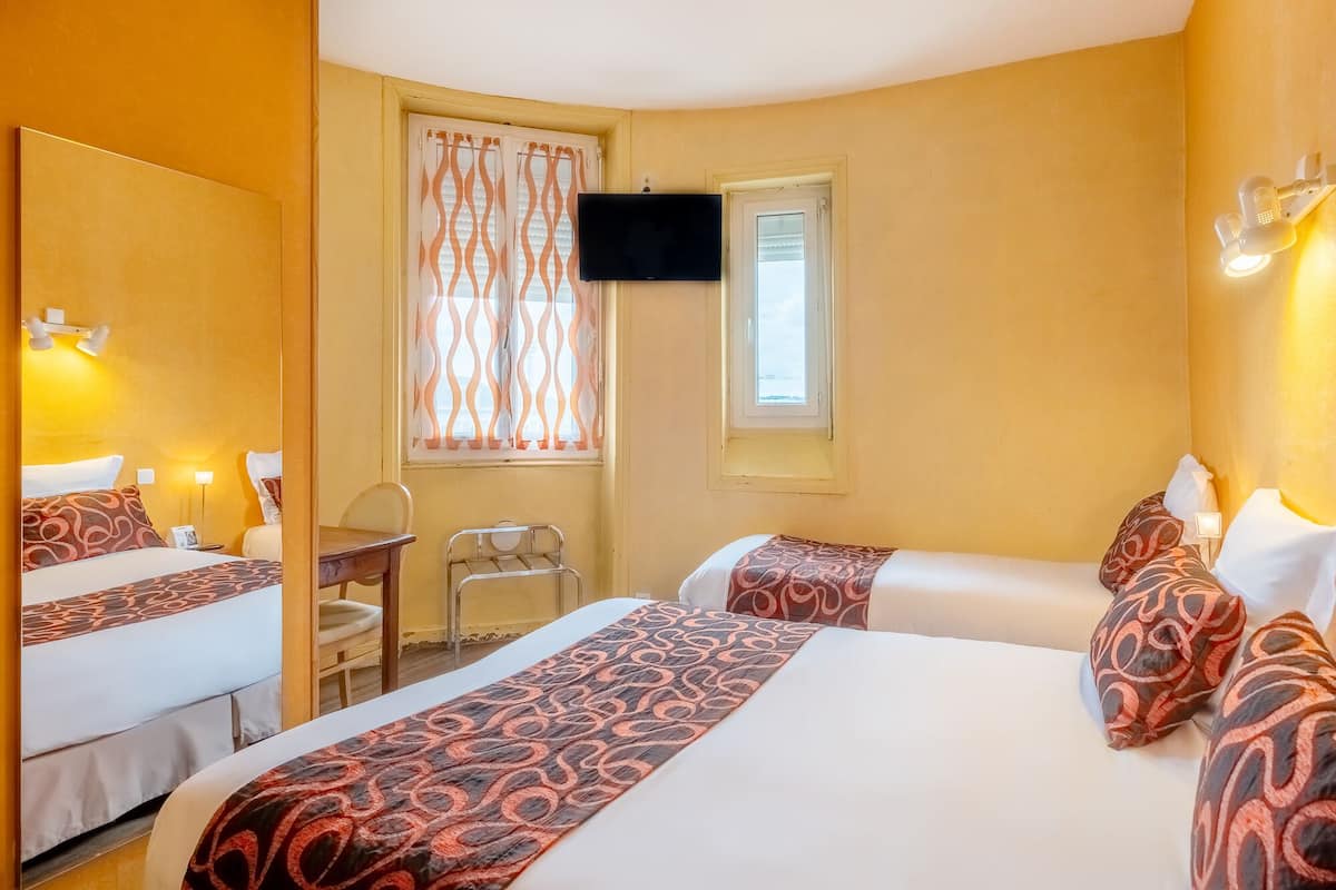 Hotelkamer met twee bedden, een bureau, een stoel, een aan de muur bevestigde televisie en een raam met gemotiefde gordijnen.