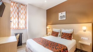 A hotel room with a large bed, two bedside tables, a radiator, and a window with orange curtains.