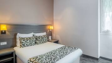 Ein Hotelzimmer mit Bett, Nachttischlampen, einem Nachttisch und einem Fenster mit Jalousien.