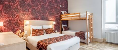 Habitación de hotel con una cama grande, una litera, un escritorio de madera y un papel tapiz floral rojo.
