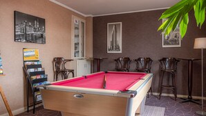 A pool table in a room with a cityscape painting, a welcome sign, and a cabinet.