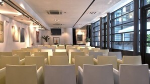 Une salle de conférence avec des rangées de chaises, de grandes fenêtres et des œuvres d’art accrochées aux murs.