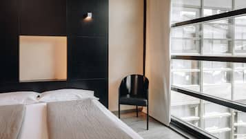 Une chambre d’hôtel moderne avec un grand lit, une chaise noire et une grande fenêtre donnant sur la ville.