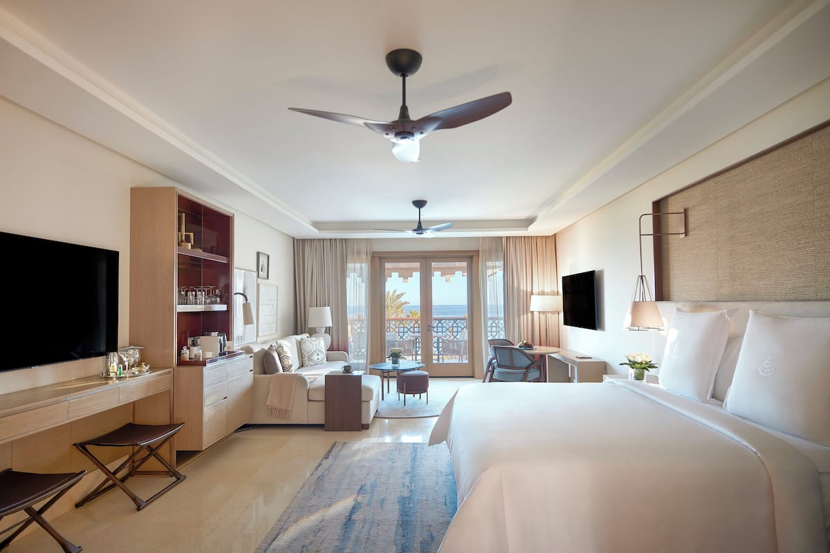 A hotel room with a bed, a desk, a chair, a TV, and a balcony with a view.
