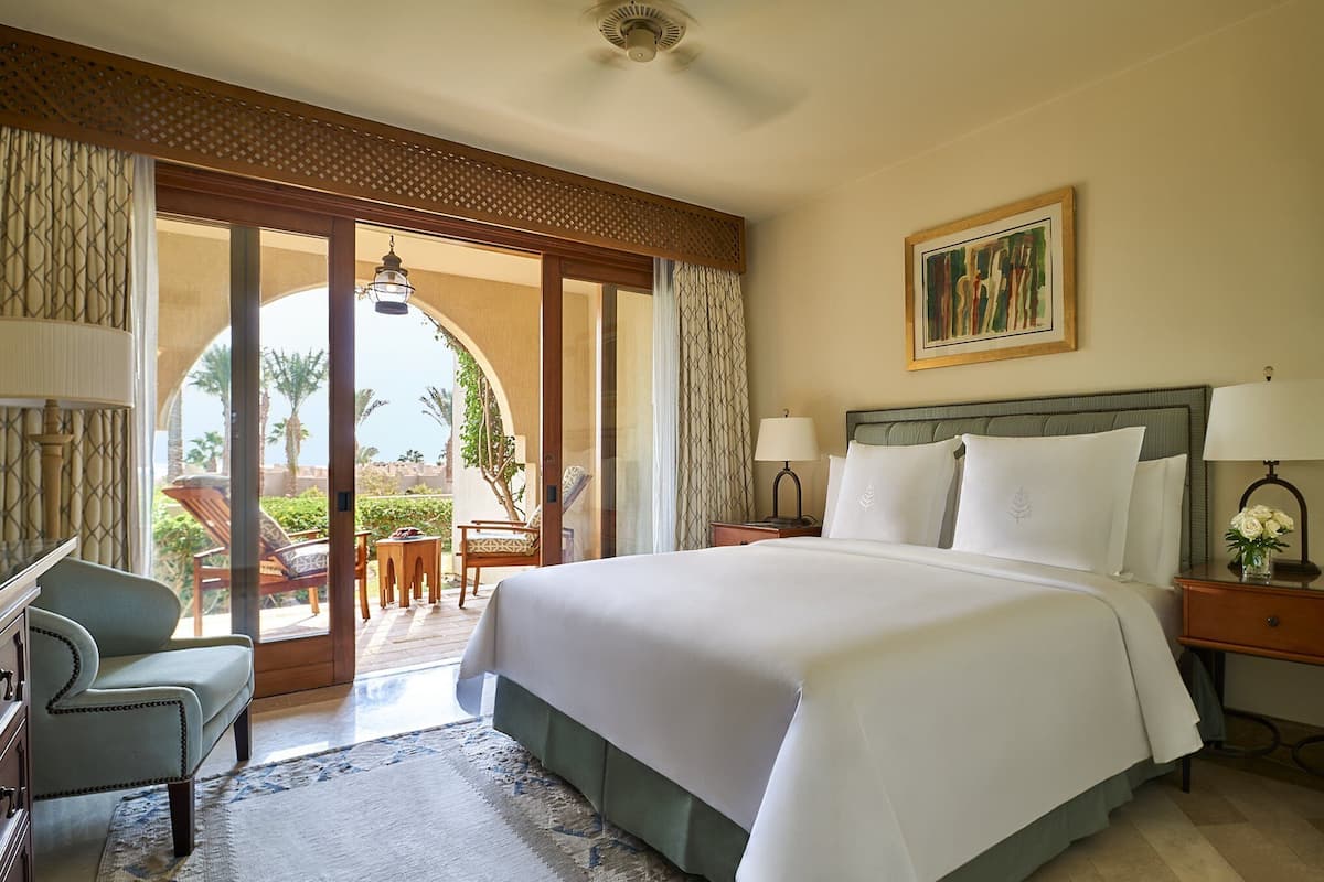 A hotel room with a large bed, a desk, a chair, and a view of the outdoors.