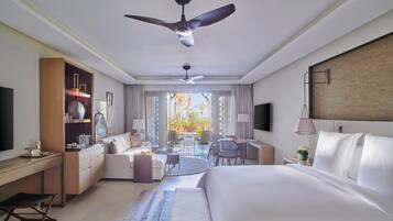 A modern hotel room with a large bed, a desk, a chair, a sofa, a dining table, and a ceiling fan.