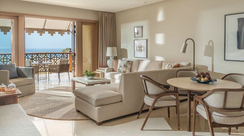 A spacious living room with a balcony overlooking the sea, furnished with sofas, a coffee table, and a dining area.