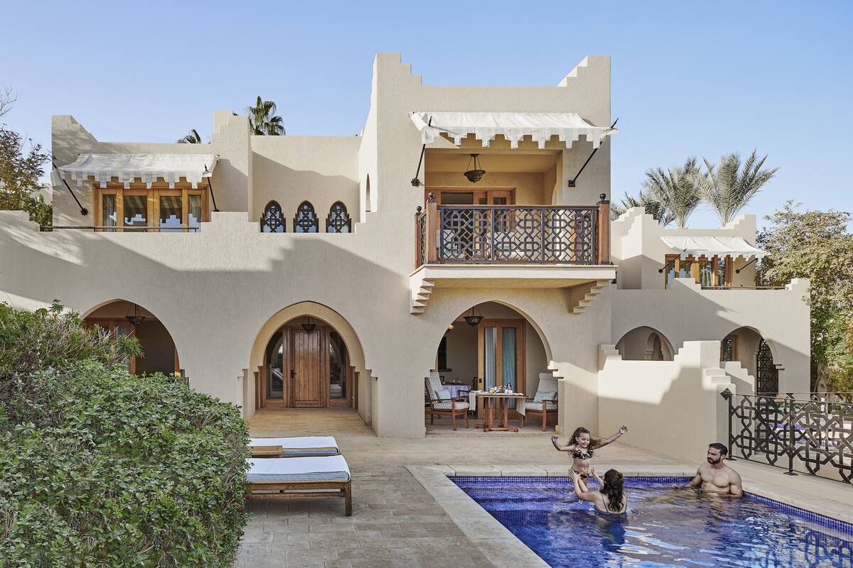 A resort with a swimming pool, outdoor seating, and a two-story building with arched doorways.