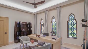 A room with a desk, chairs, a bookshelf, and large windows with decorative glass panes.