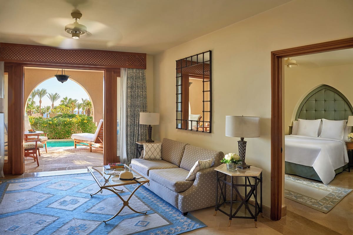 A hotel room with a sofa, a small table, a bed, and a view of the outdoors.