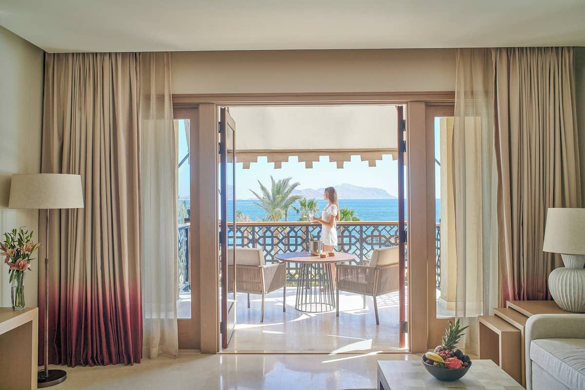 A hotel room with a balcony, a dining table, and a view of the sea.