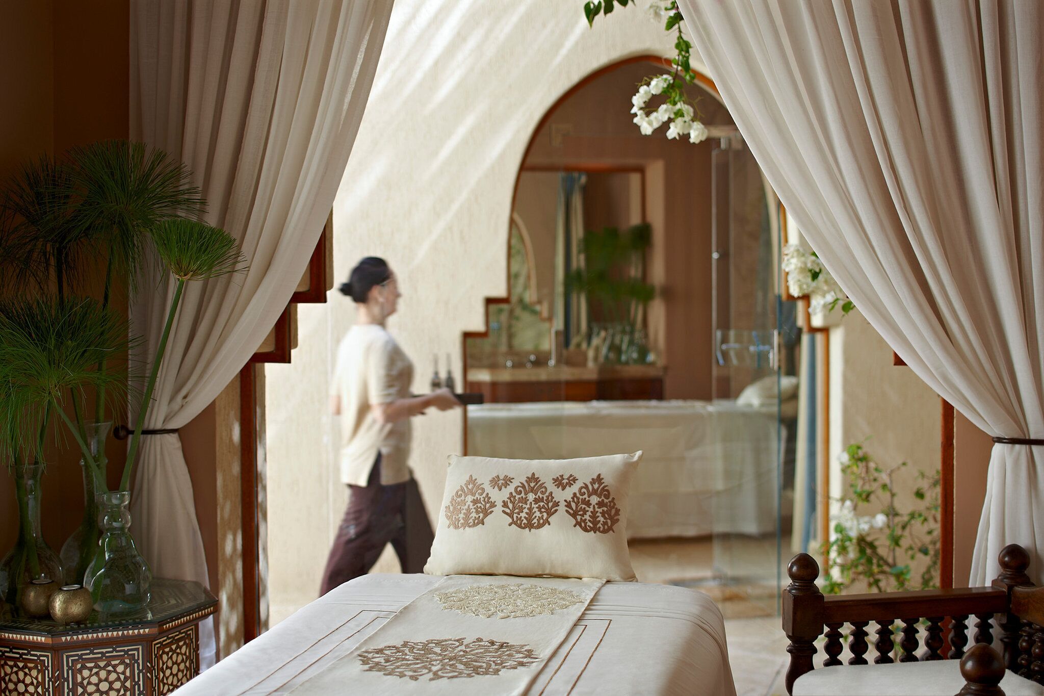 A bedroom with a bed, a nightstand, a mirror, and a window with curtains.